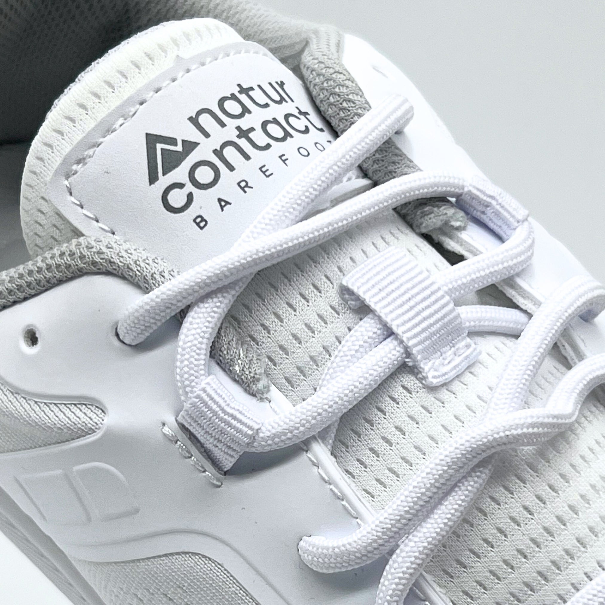 detail of white barefoot trainers with naturcontact logo in studio with white background