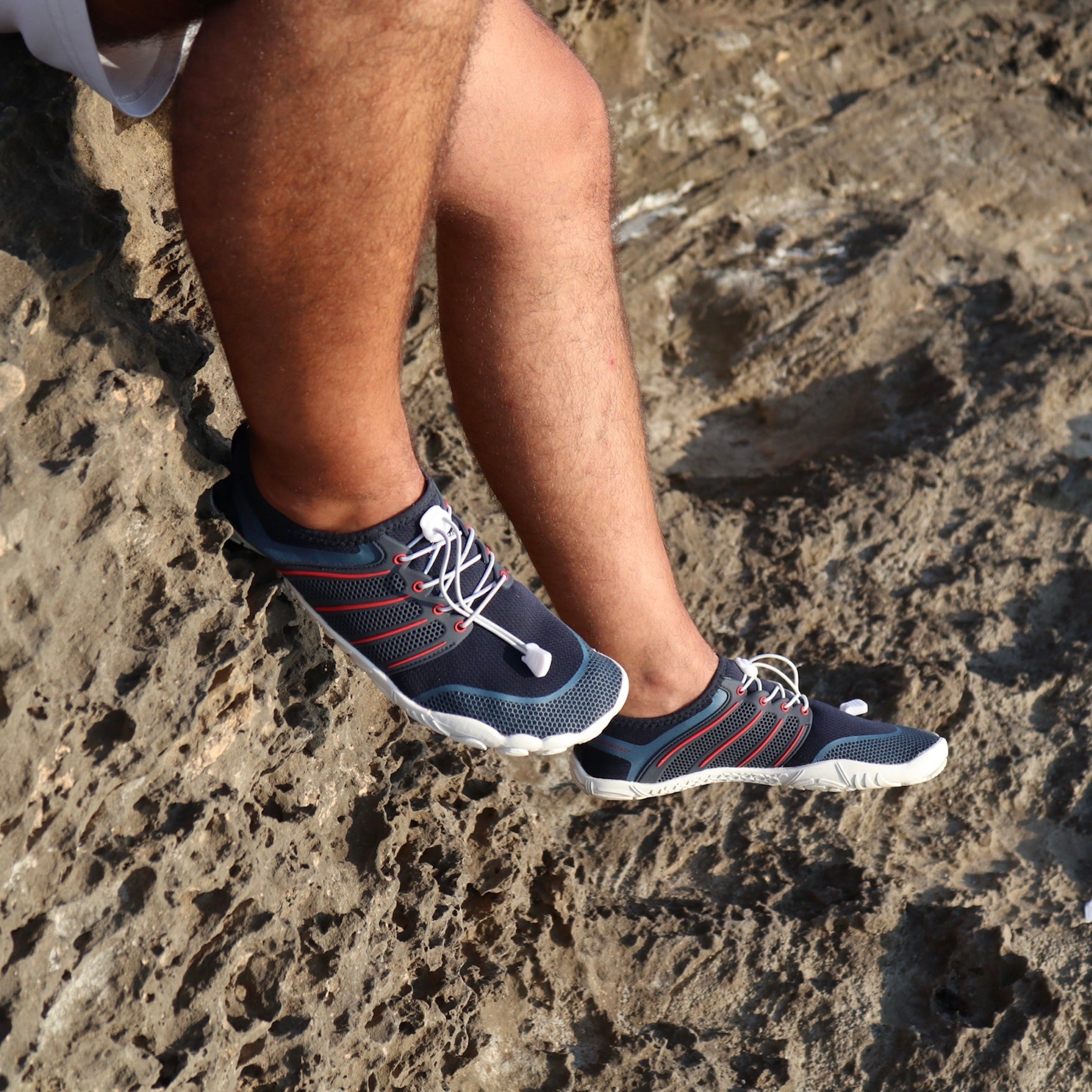 blue and red summer barefoot shoes with white soles on beach rocks