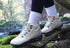 White hiking barefoot boots worn with black leggings and white socks, standing on a log in a forest setting.