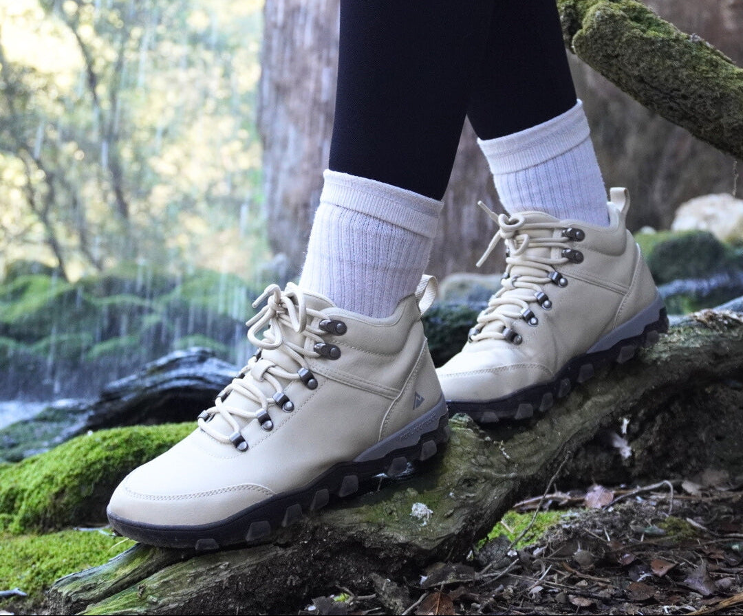 White hiking barefoot boots worn with black leggings and white socks, standing on a log in a forest setting.