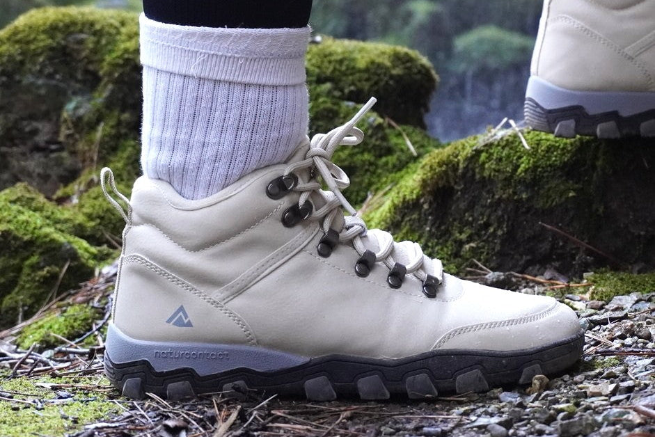 White hiking boots with black soles on a person standing on a mossy ground.