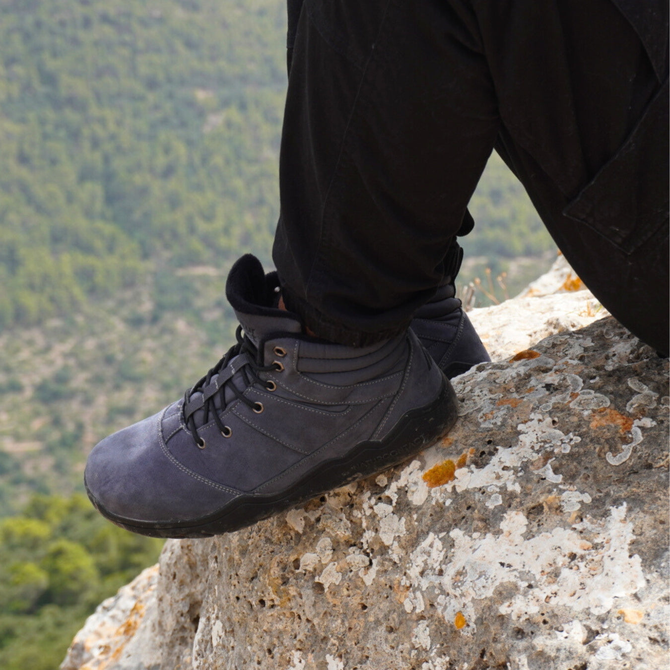 Person wearing gray hiking boots on a rocky outcrop with a mountainous background