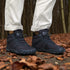 Navy hiking boots with visible brand logo worn on a forest floor.
