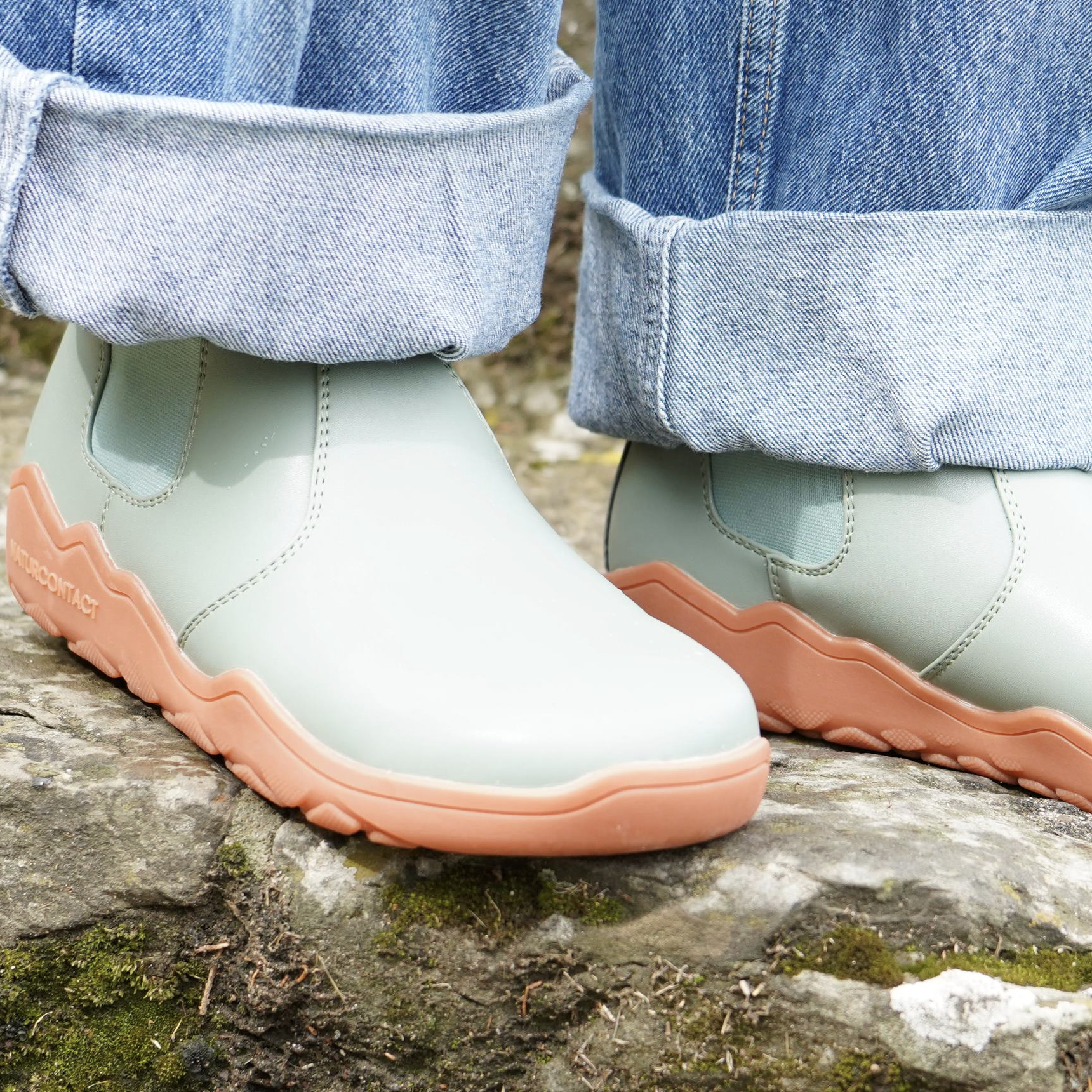 detail of green barefoot chelsea boots from top with orange sole on a rock