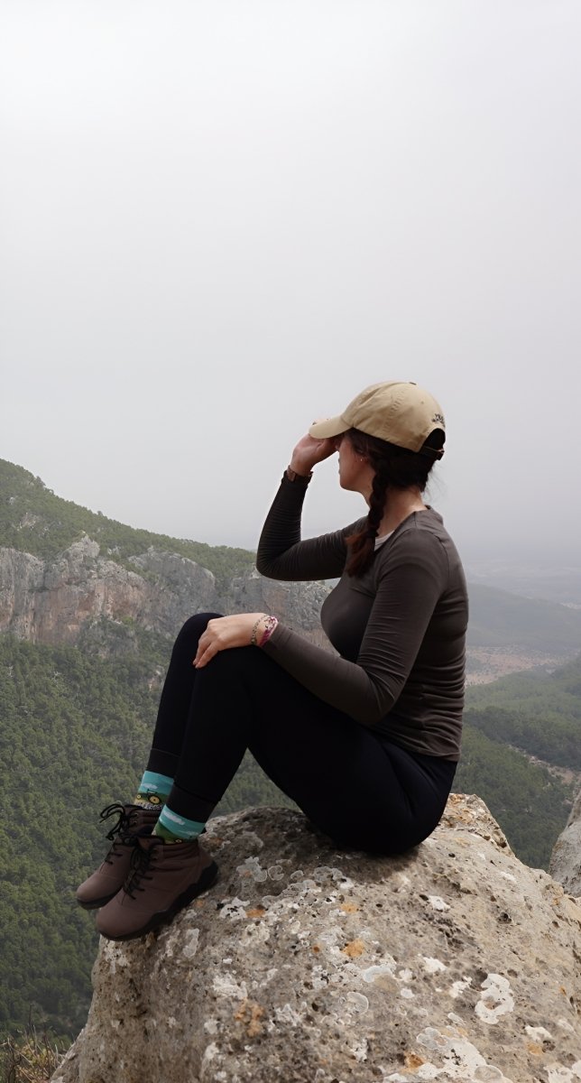 Person sitting on a rocky outcrop overlooking a mountainous landscape on a foggy day with intemperia 2.0 barefoot hiking shoes