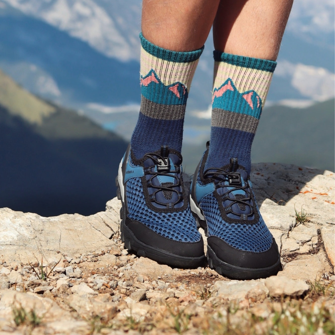 Person wearing blue hiking shoes and socks with mountain design in a mountainous landscape