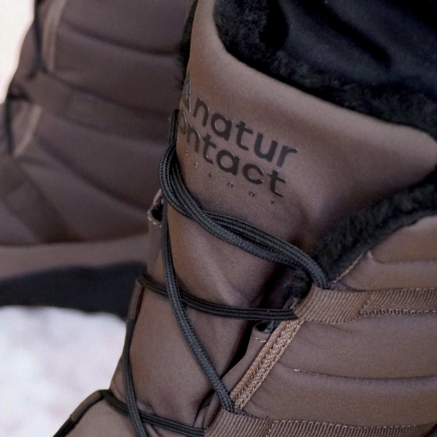 Close-up of brown Naturcontact winter boots with black laces and black faux fur lining, showing detailed stitching and padded design