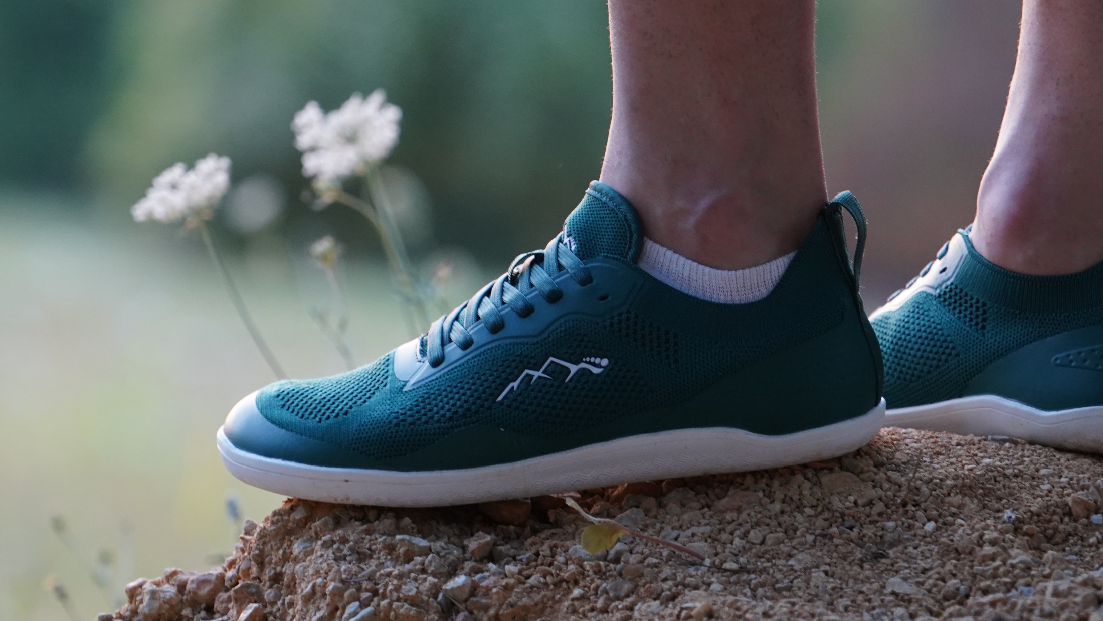 Person wearing Naturcontact barefoot shoes standing on a log in a forest, demonstrating natural movement and ground feel.