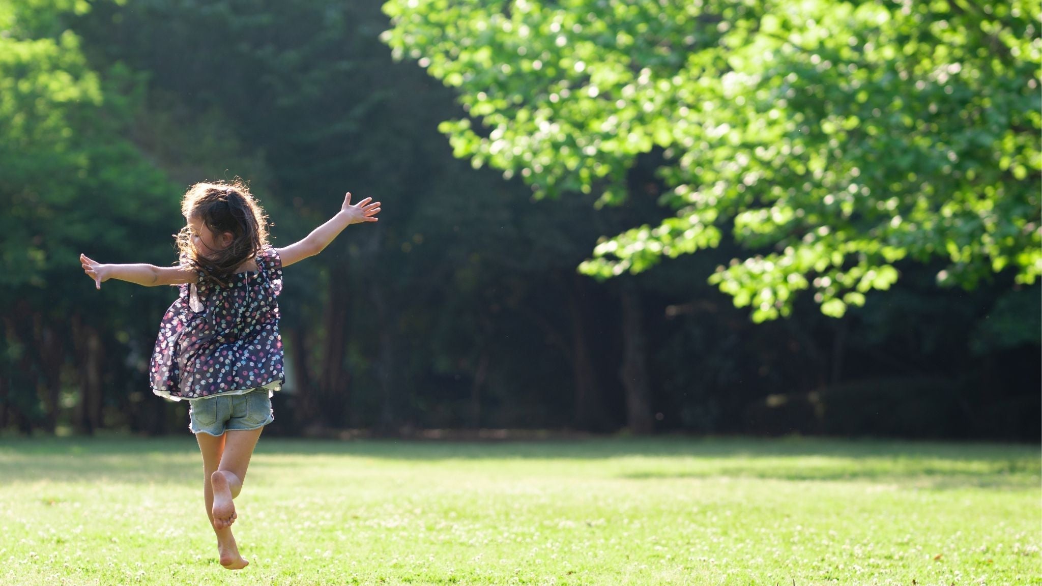 Child running barefoot in the grass on a sunny day, symbolizing natural movement and freedom.