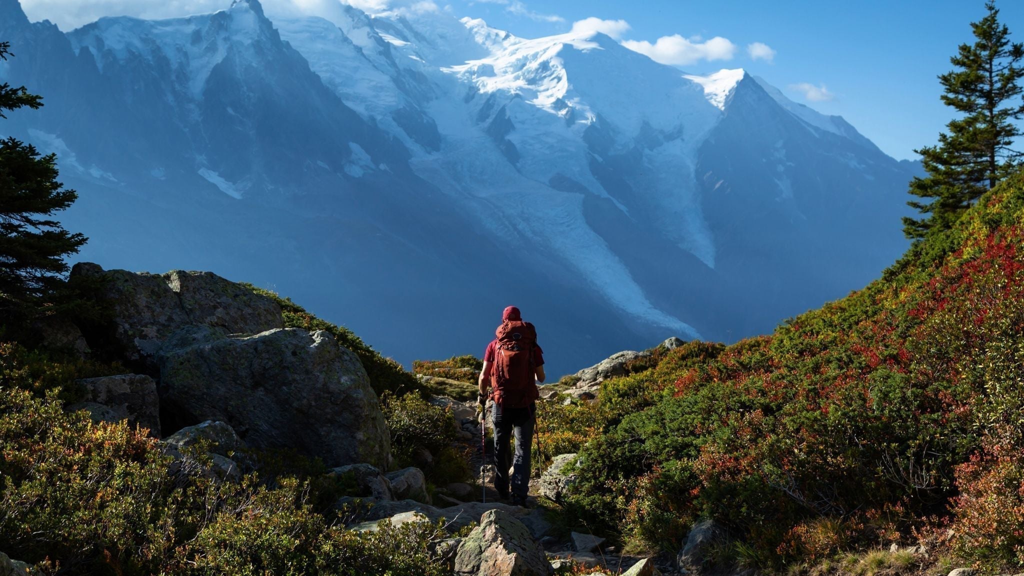 Hiker standing on a rocky peak with a backpack, overlooking high-altitude