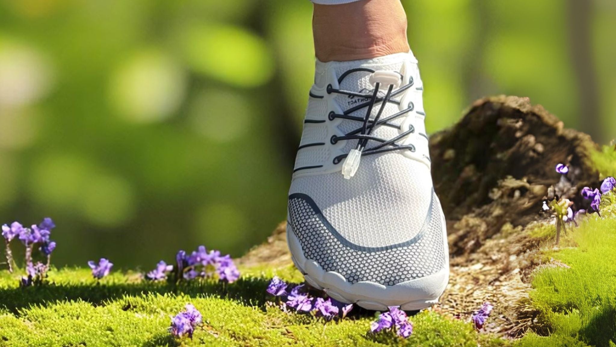 White Naturcontact barefoot shoe with elastic black laces stepping on grass and wildflowers, symbolizing natural walking and balance.