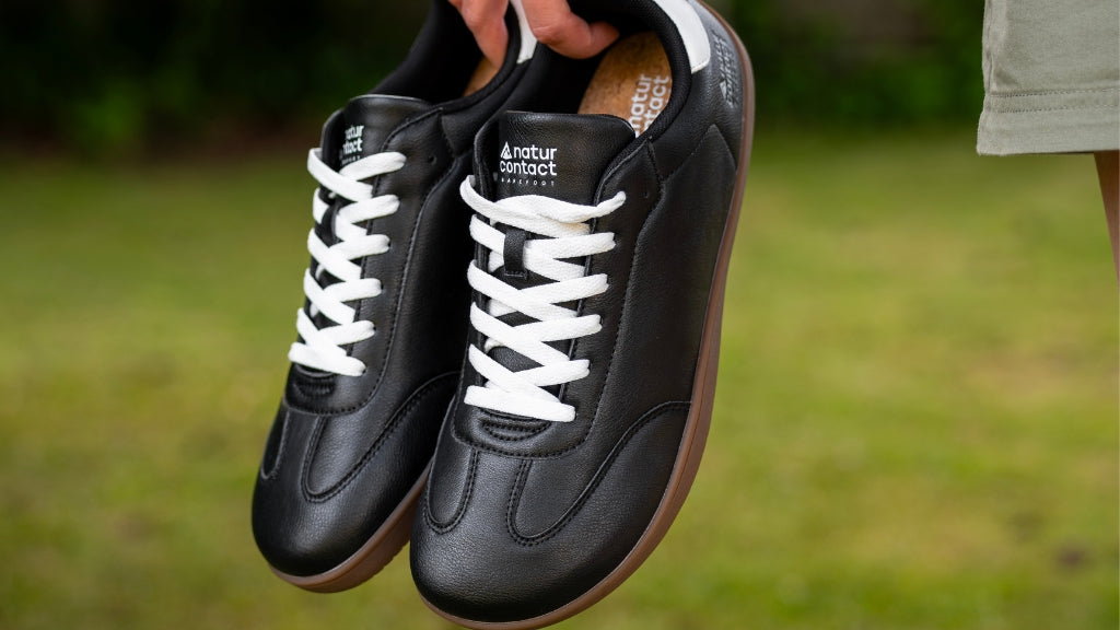 Black barefoot trainers with a wide toe box and zero-drop sole held outdoors
