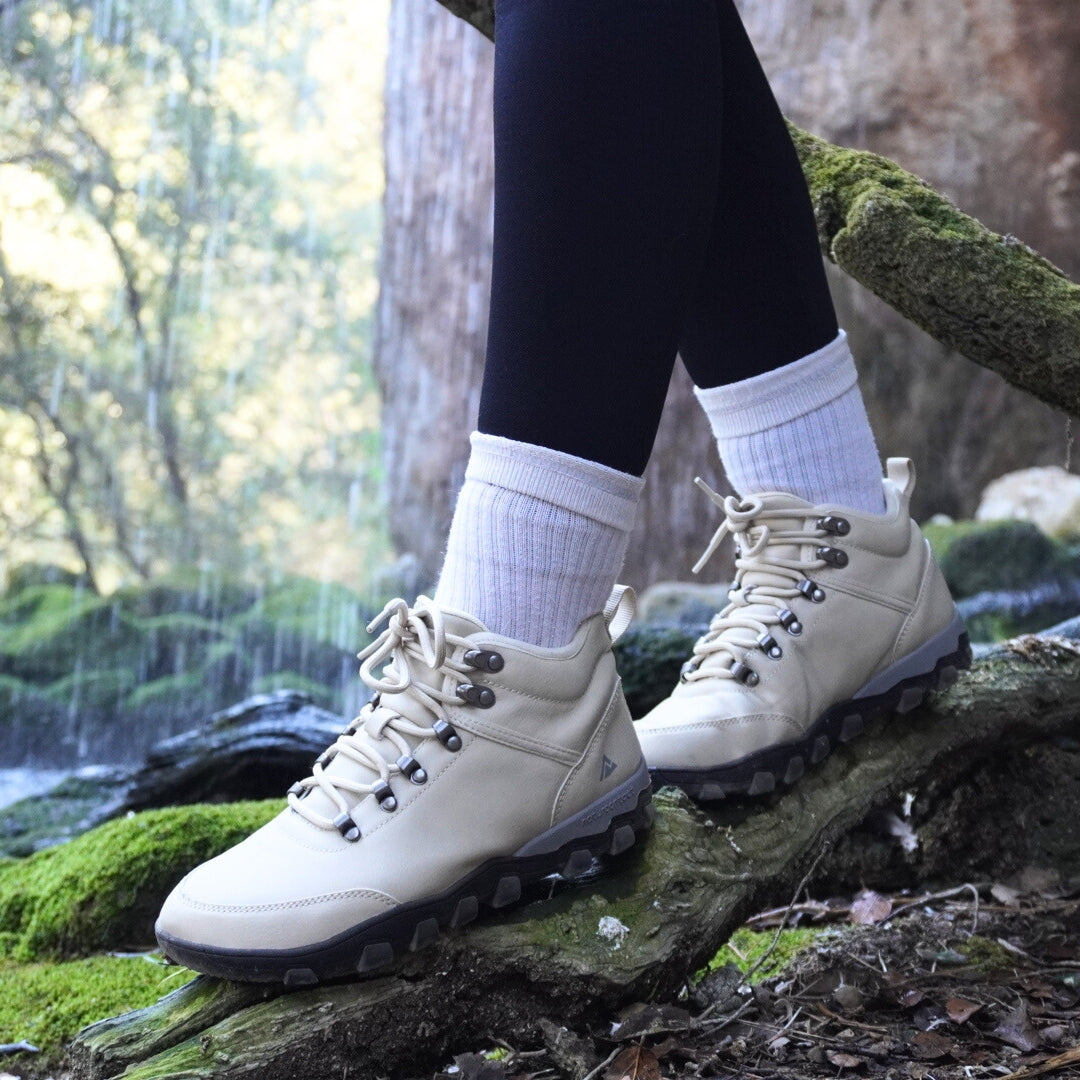 White hiking barefoot boots worn with black leggings and white socks, standing on a log in a forest setting.