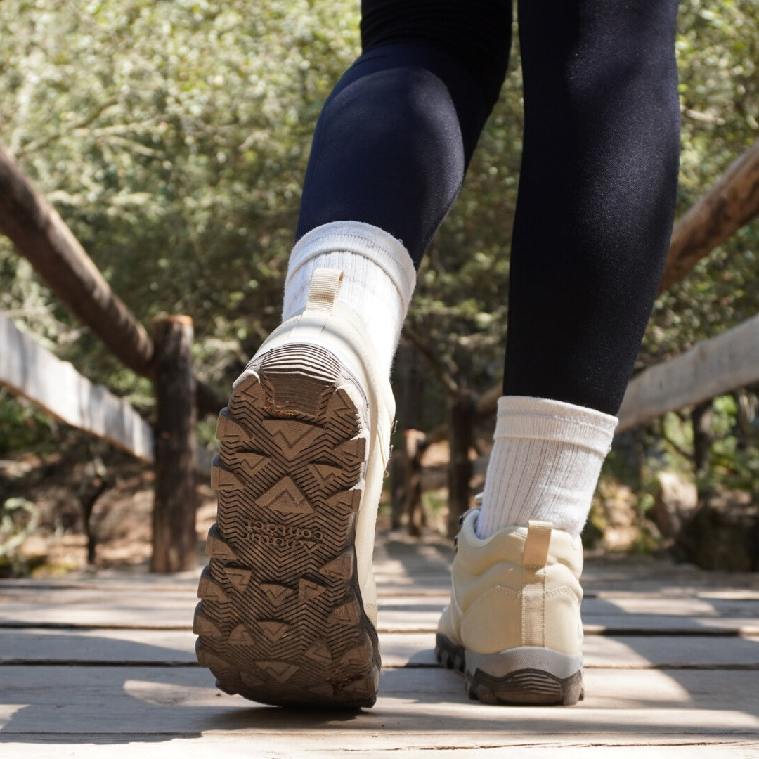 Close-up of feet wearing white barefoot boots with brown soles on a wooden path with trees in the background