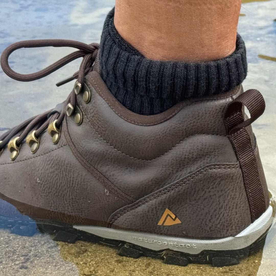 Brown hiking barefoot boot with a brand logo worn by a person on a natural background