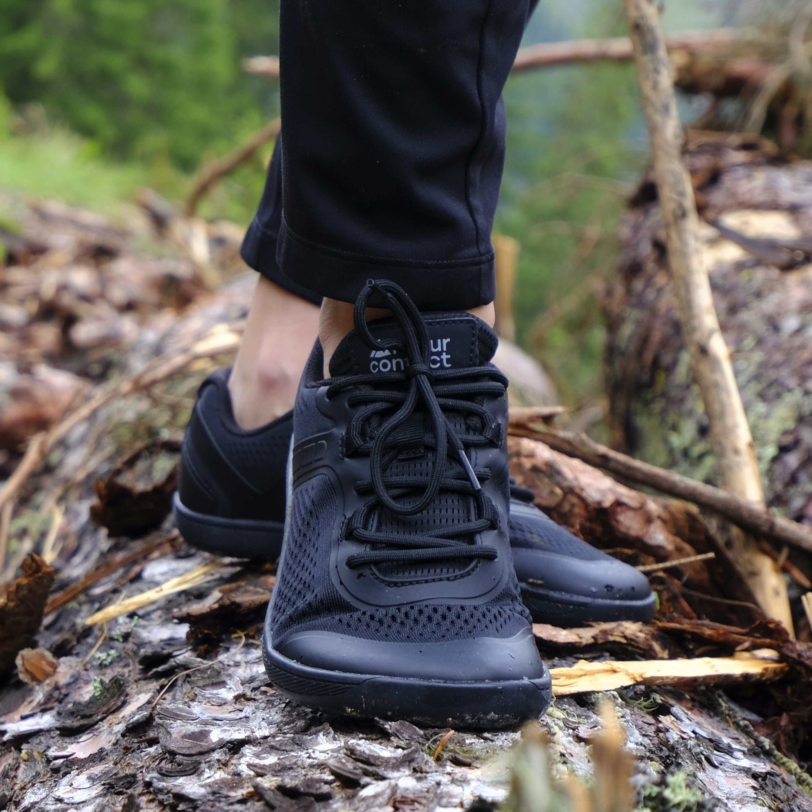 Black Metro Flex barefoot shoes for training worn on a forest floor with blurred background