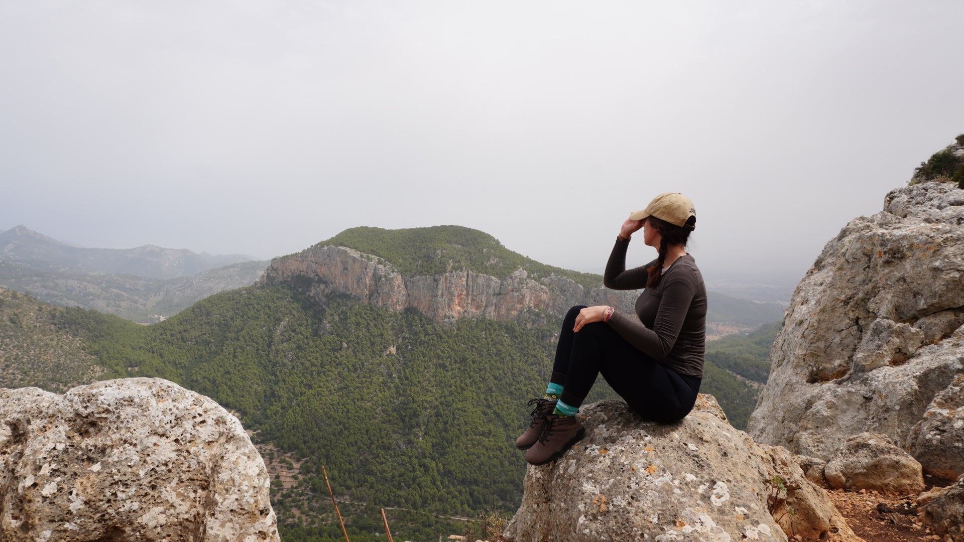 Person sitting on a rocky outcrop with a mountainous landscape in the background and wearing outdoor barefoot shoes