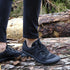 Person wearing black sneakers standing on a log in a forest setting