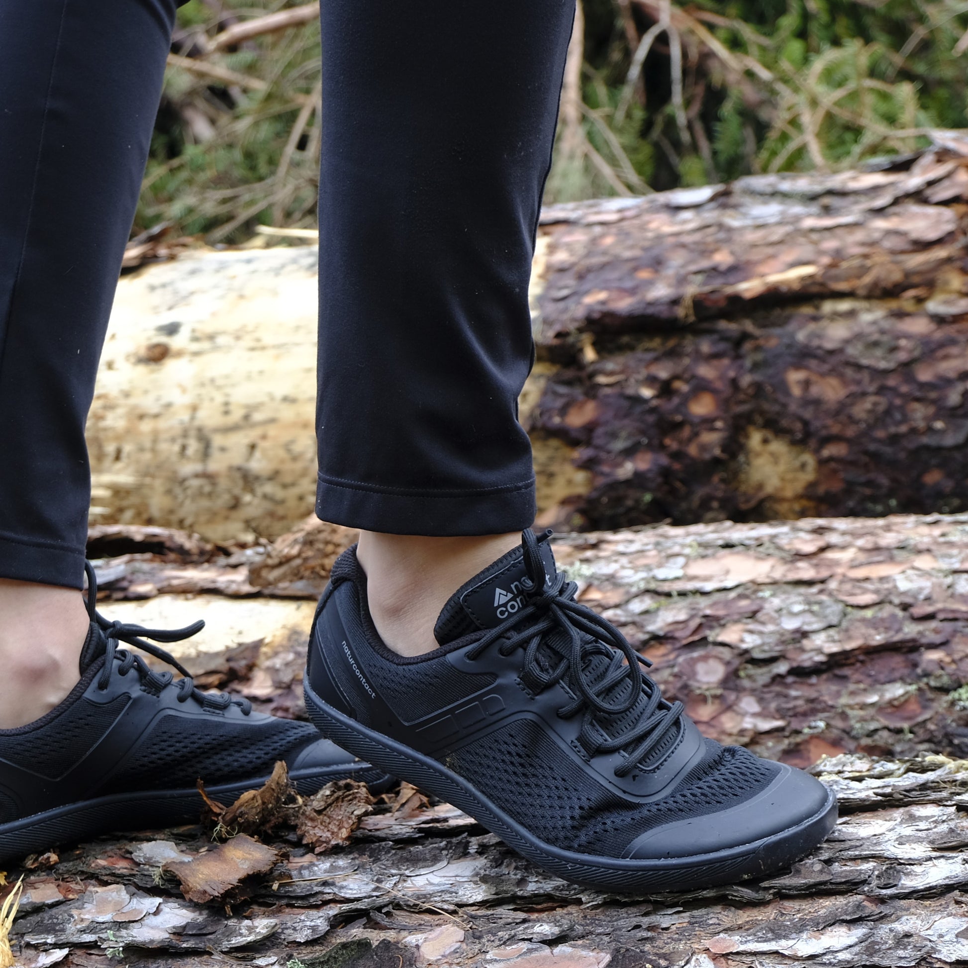 Person wearing black sneakers standing on a log in a forest setting