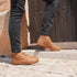 Person wearing brown leather smart barefoot shoess and dark jeans standing on stone steps.