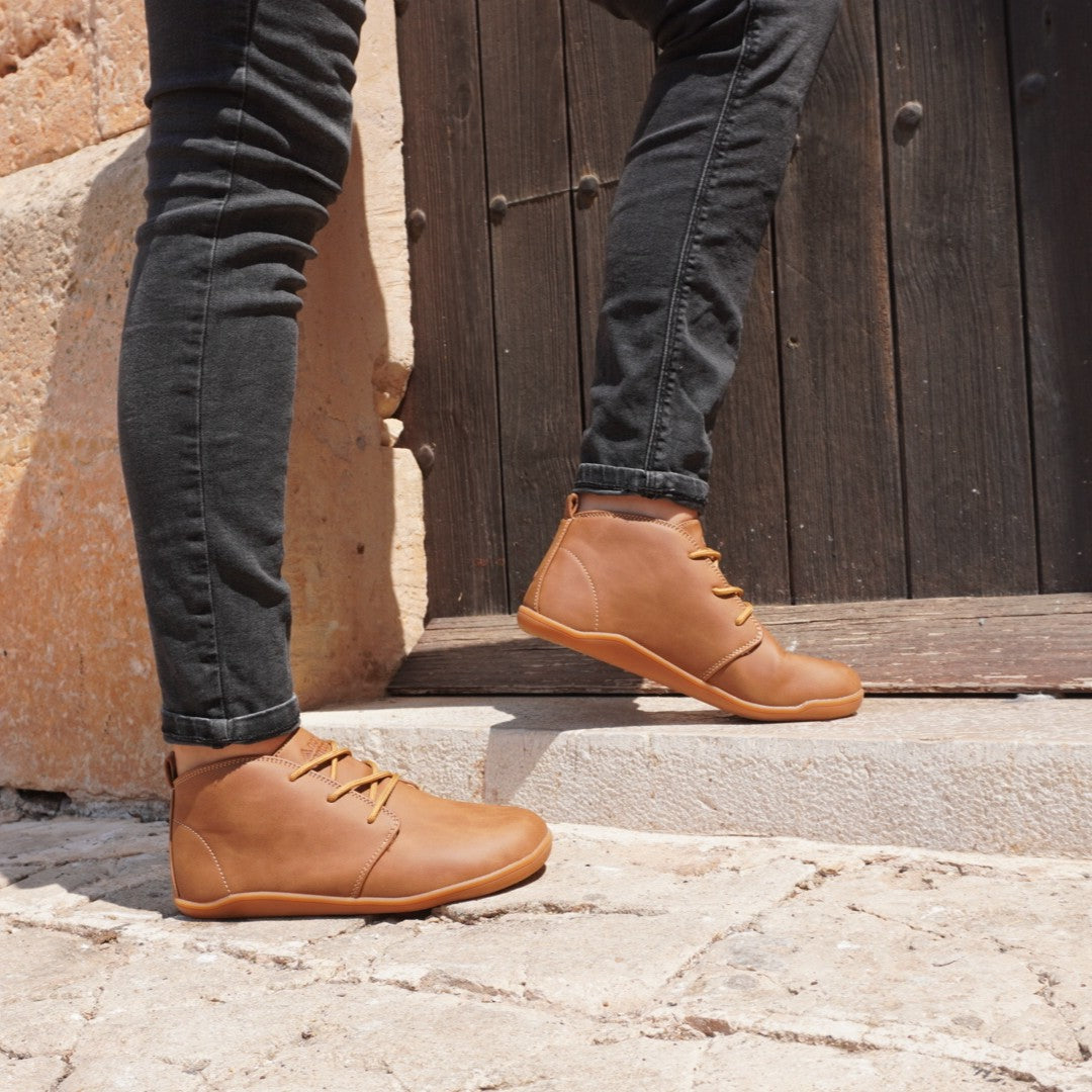 Person wearing brown leather smart barefoot shoess and dark jeans standing on stone steps.
