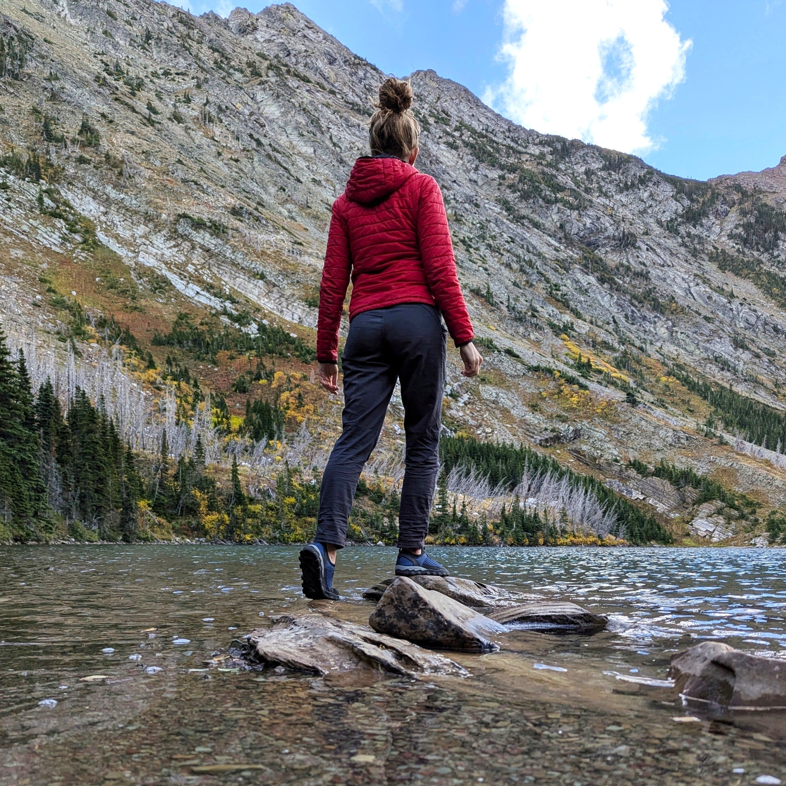 Person in a red jacket standing on rocks in a mountain lake