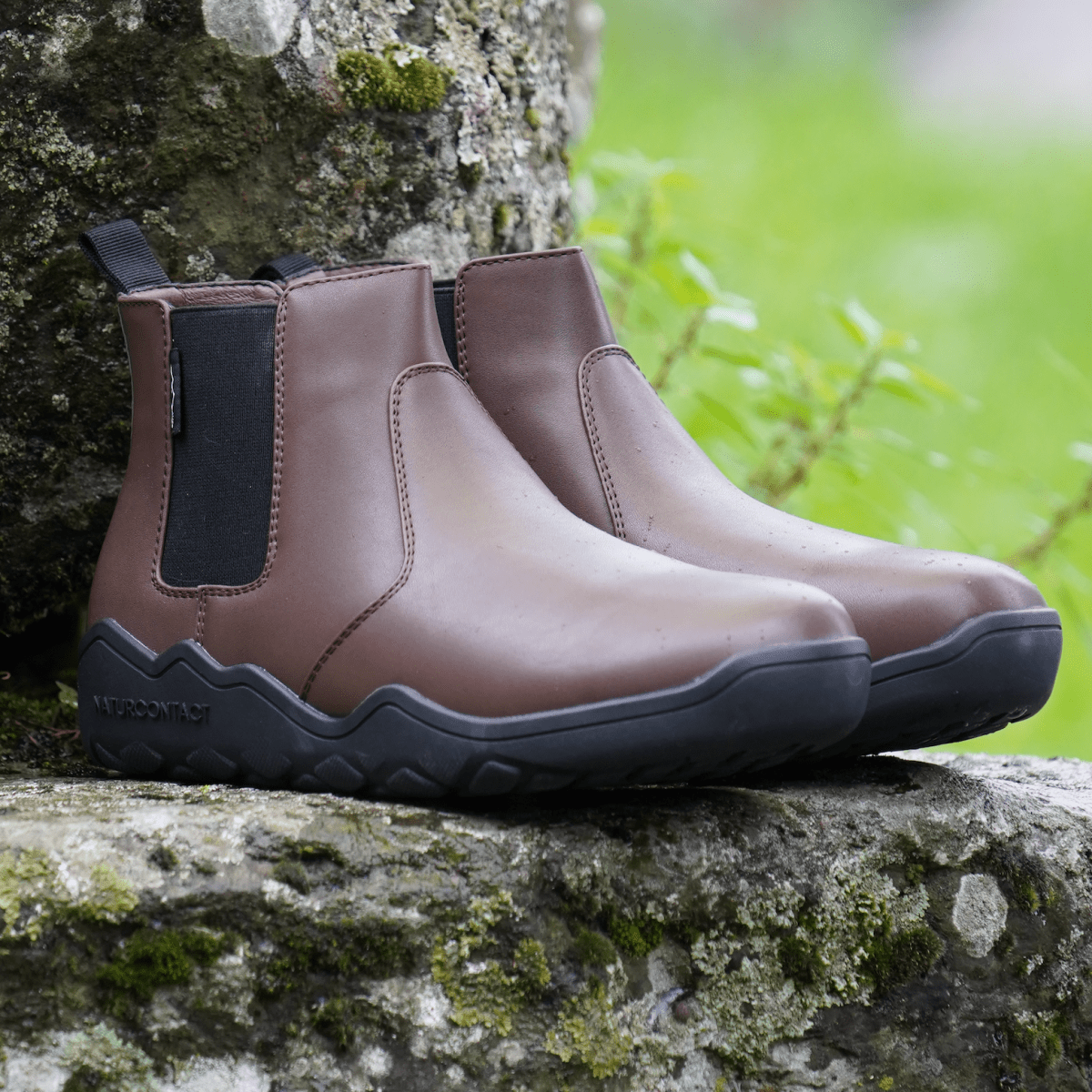 side view of Coffee minimalistic barefoot chelsea boots on a rock