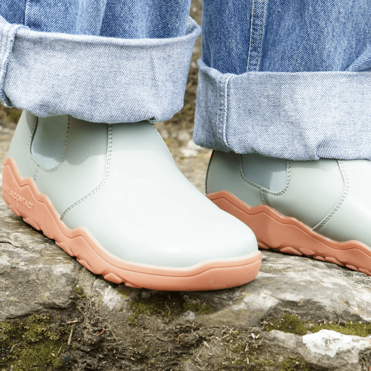 detail of Sage Green barefoot chelsea boots from top with orange sole on a rock