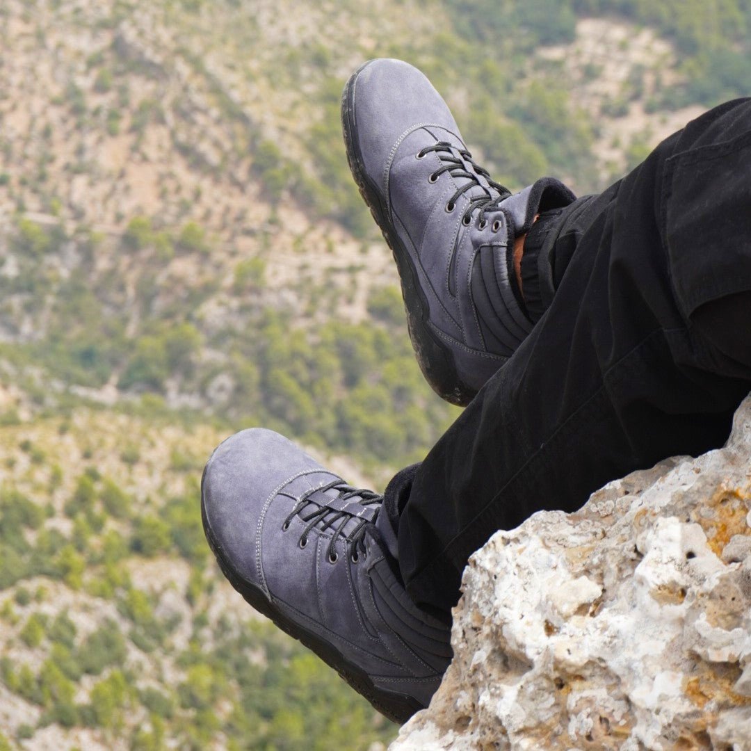 Person wearing black hiking barefoot boots sitting on a rock with a mountainous background