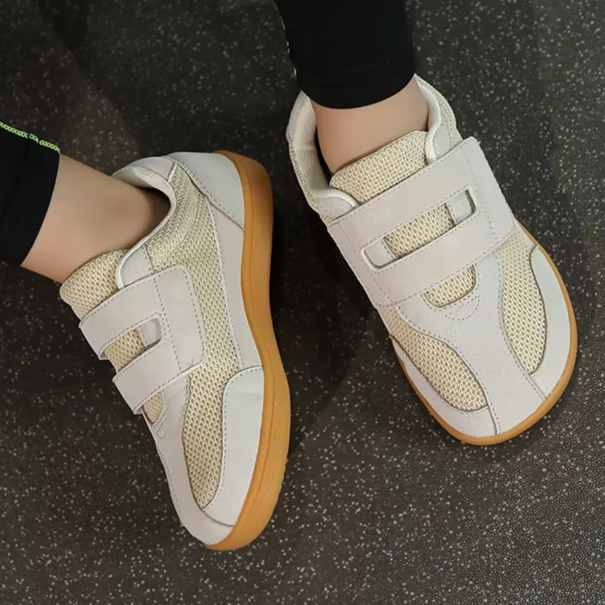 beige barefooot sneakers for kids with brown soles on a dark textured surface