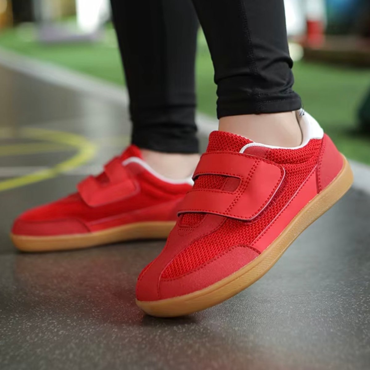 Red barefoot sneakers with velcro straps worn by a kids on a reflective floor.