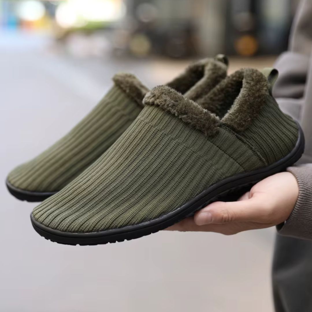 Green barefoot slippers with fur and rubber black sole on hand with blurred background