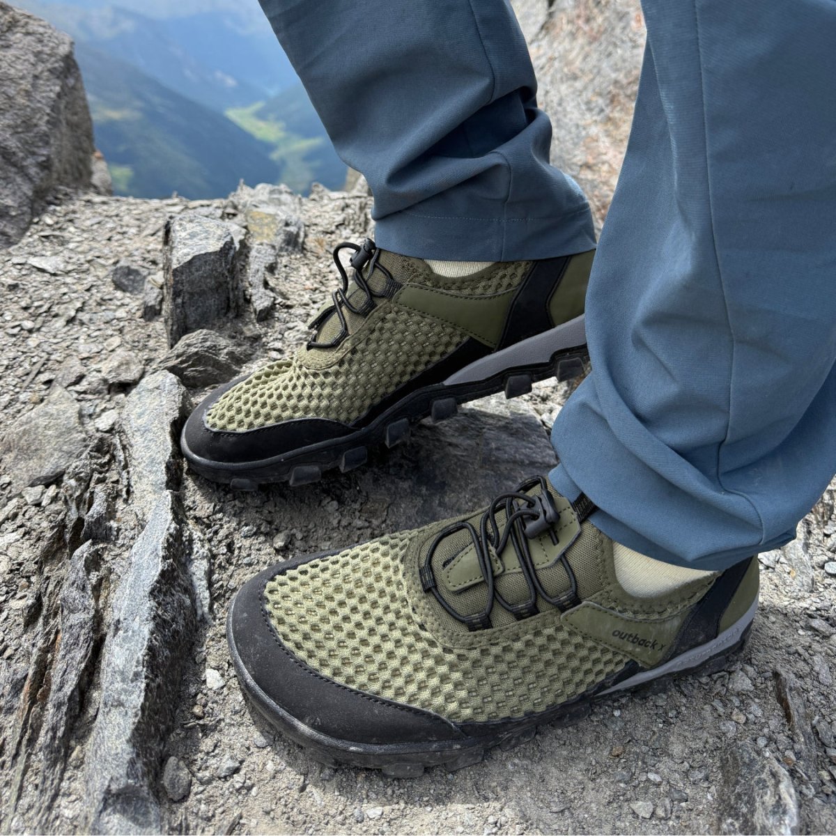 Green hiking shoes on rocky terrain with a mountainous background