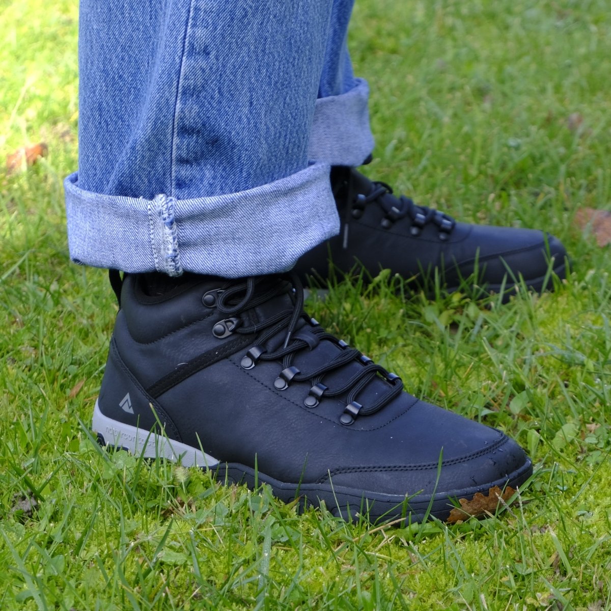 Black boots worn with rolled-up jeans on a grassy background