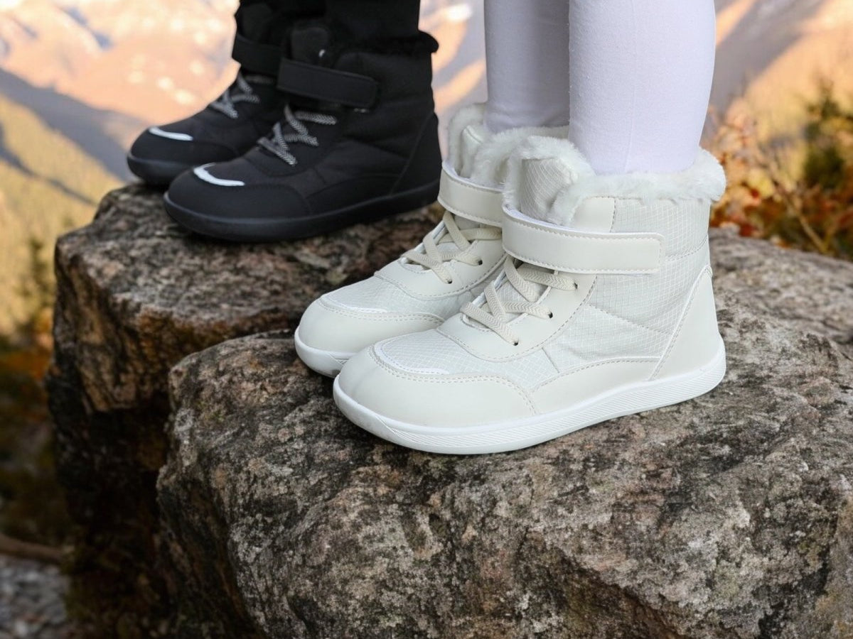Naturcontact Winter Mini Contact kids barefoot winter boots in White and Black worn outdoors on rocks, featuring fleece lining, high ankle support, adjustable strap, lace closure, and flexible minimalist sole