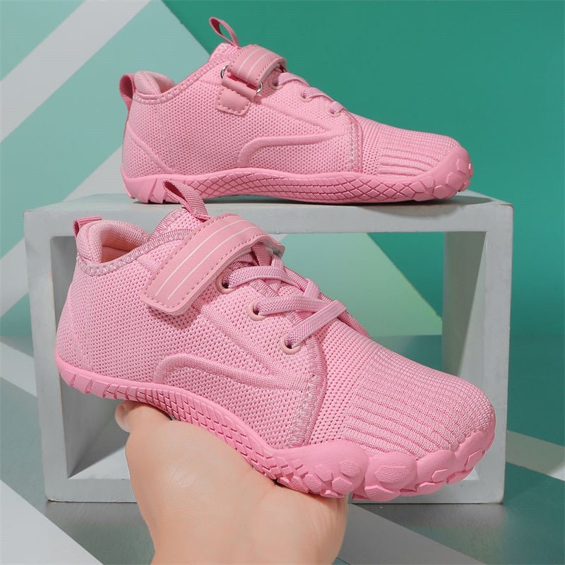 Pink children's barefoot sneakers on a geometric patterned background