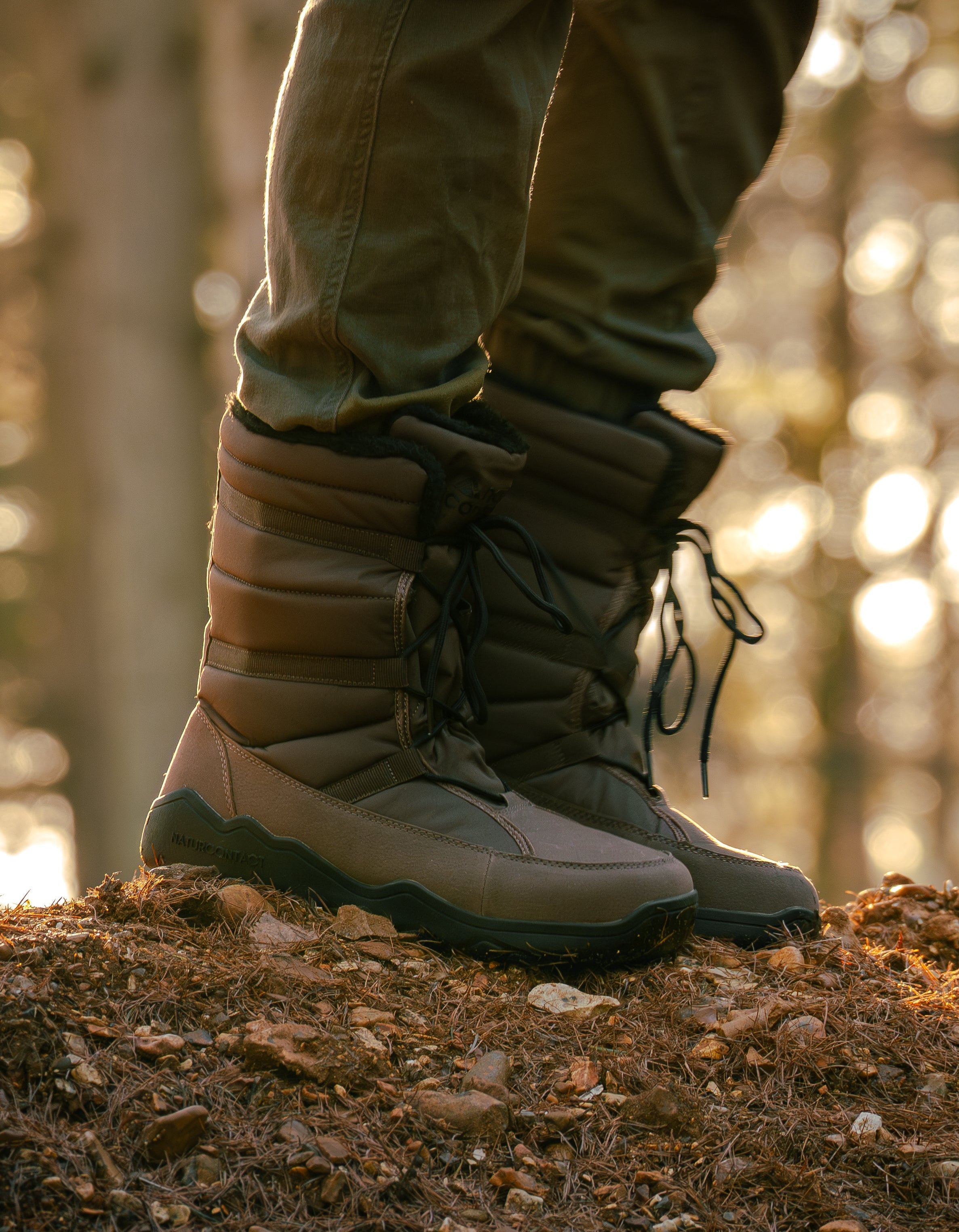 Person wearing brown winter boots on a forest floor with blurred background