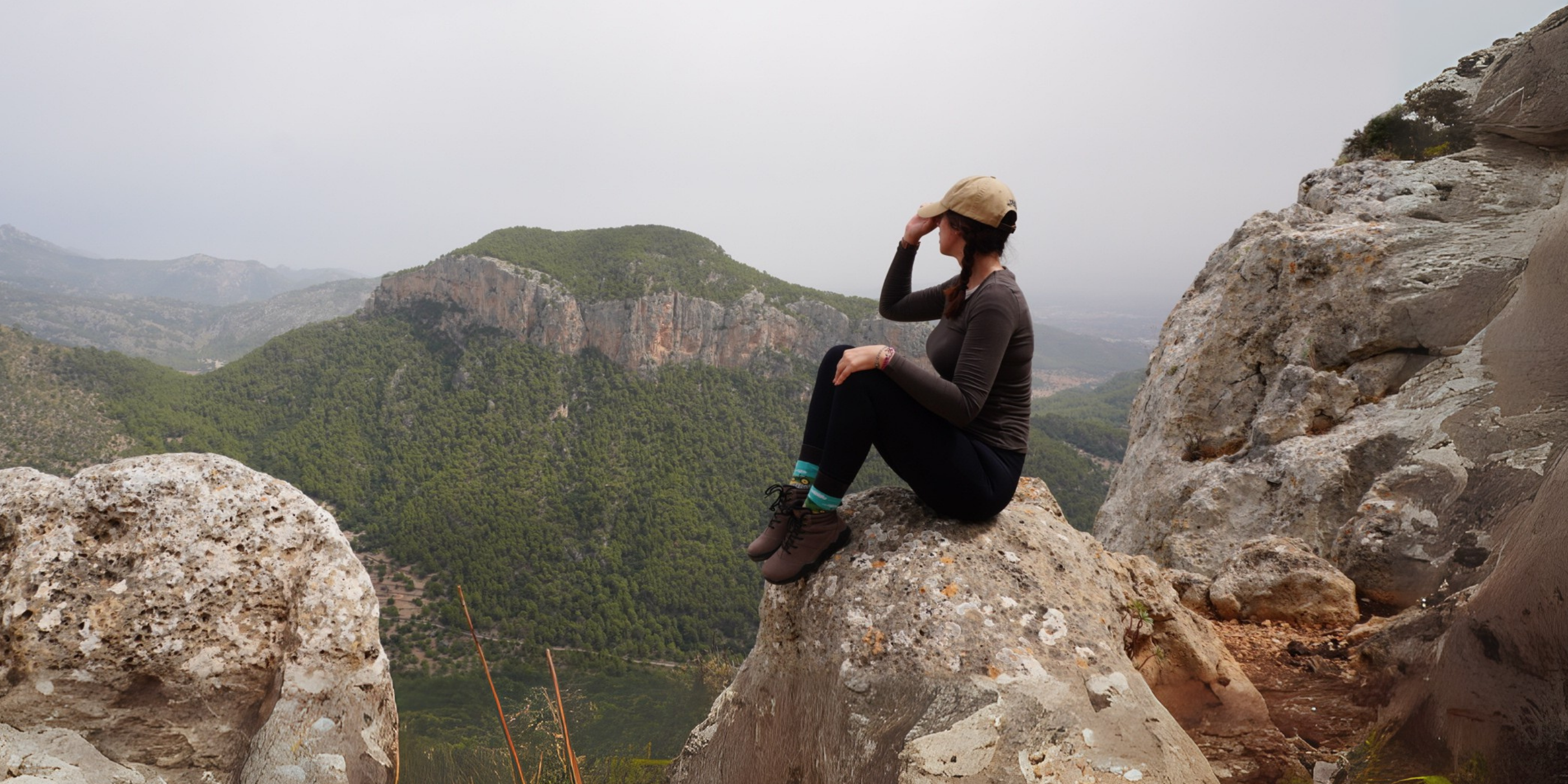 Person sitting on a rock with a scenic mountain view in the background
