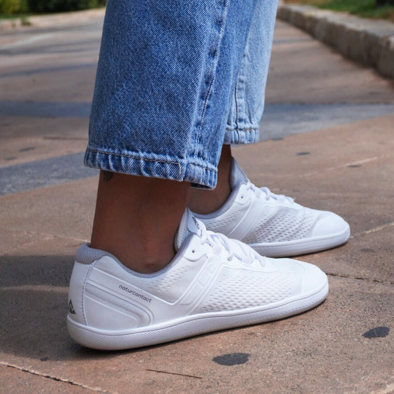White sneakers worn with rolled-up blue jeans on a pavement.