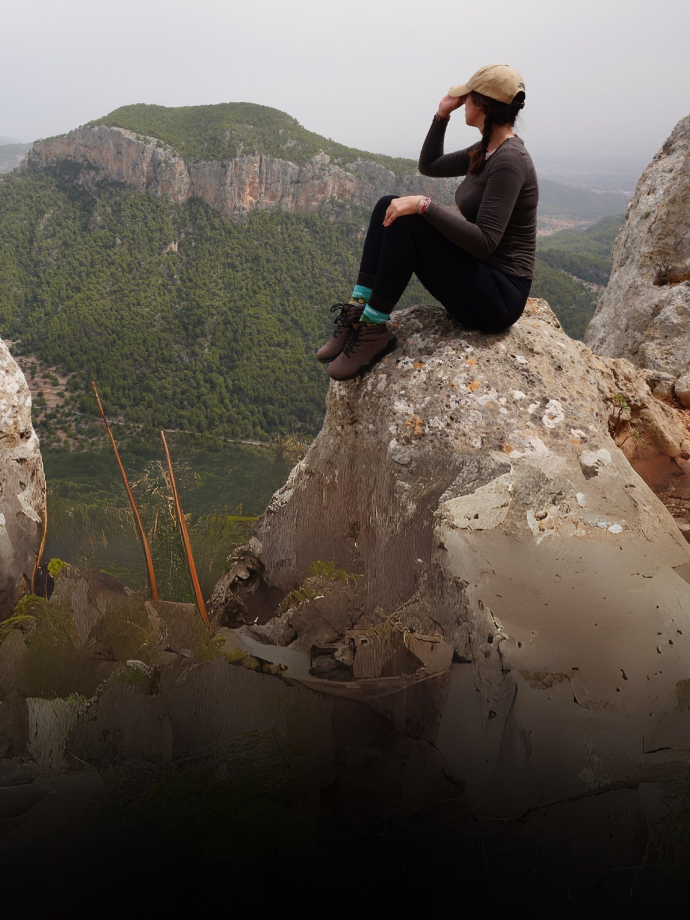 Person sitting on a rocky outcrop with a mountainous landscape in the background