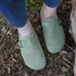 Person wearing mint green suede clogs with a buckle on a stone path.