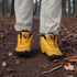 Gold hiking boots with black soles worn by a person in a forest setting.