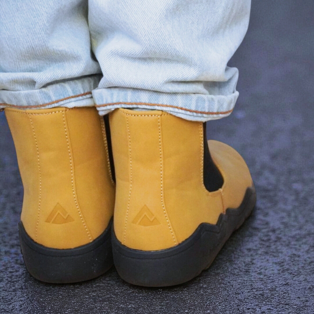 Sand slip-on shoes with black soles worn with light blue jeans on a dark surface.