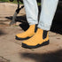 Yellow boots with black soles worn by a person on a sidewalk.