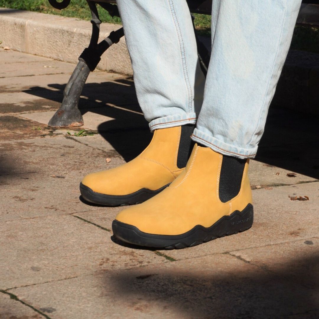 Yellow boots with black soles worn by a person on a sidewalk.