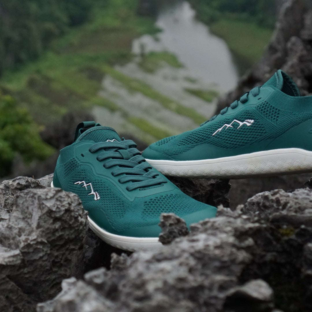 Teal running shoes with white soles on a rocky surface with a natural landscape in the background