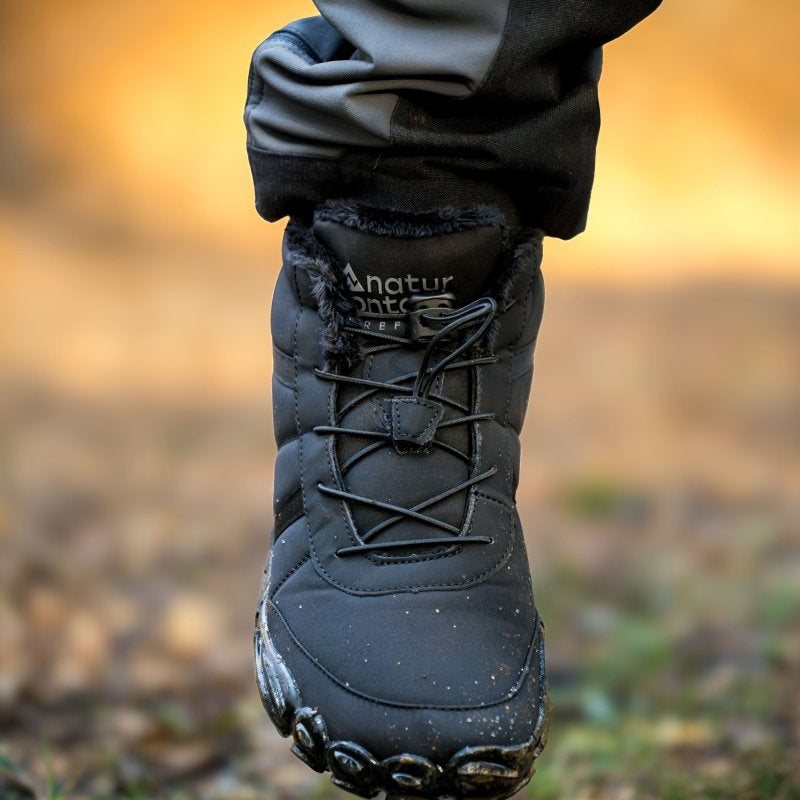 Black hiking barefoot boot with brand name naturcontact on a blurred natural background