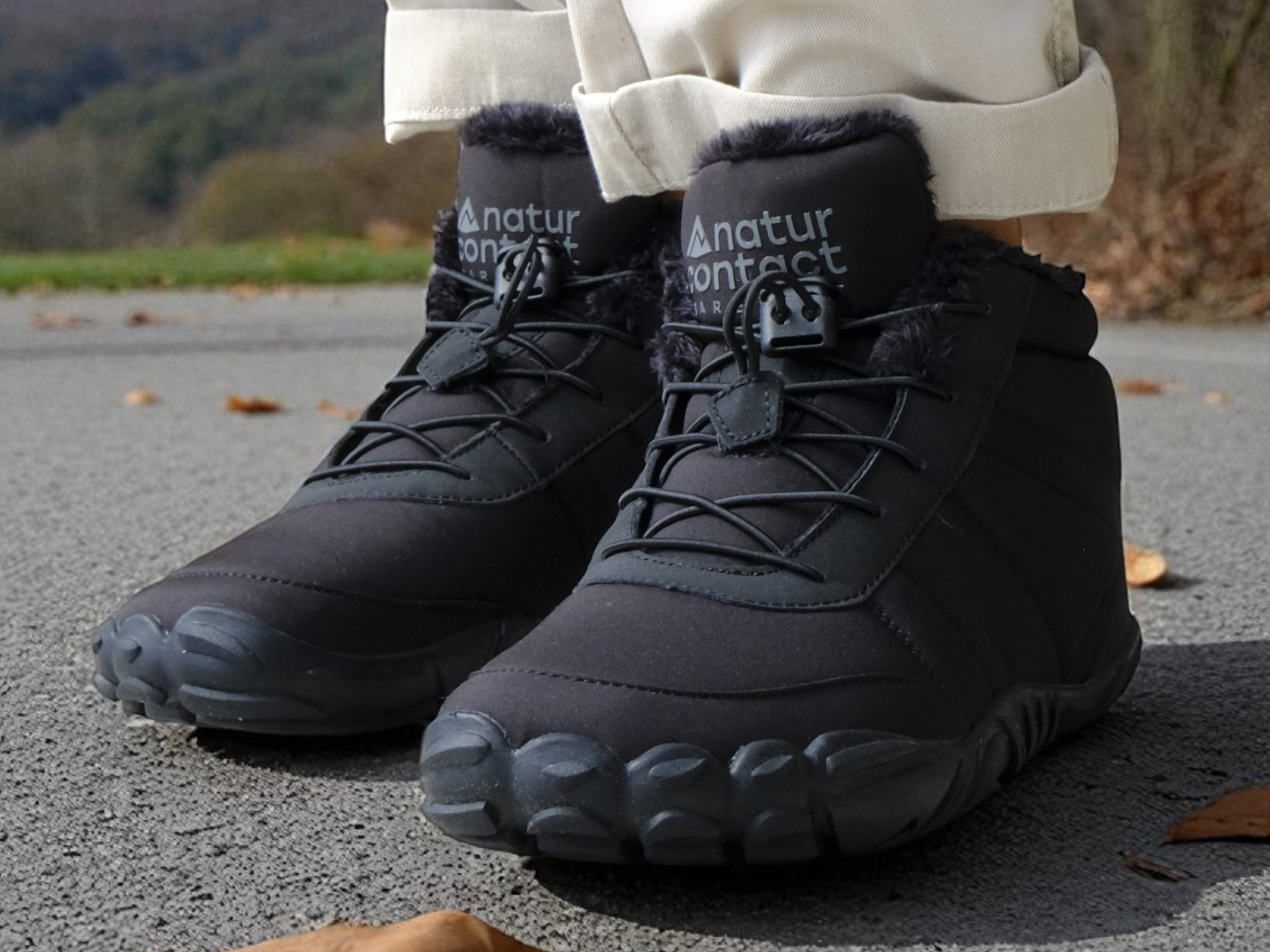 Black winter boots with fur lining worn by a person on a road with mountains in the background