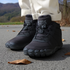 Black winter boots with fur lining worn by a person on a road with mountains in the background