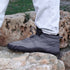 Person wearing gray hiking boots with black soles on a rocky surface
